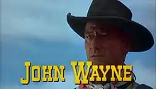 Image de film montrant en gros plan le visage d'un homme portant un chapeau de cow-boy, avec le texte « John Wayne » en lettres capitales jaunes en-dessous