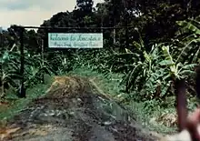Une route en terre mène sous une arche dont le panneau indique « Welcome to Jonestown ».