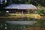 Bâtiment bas et large avec un toit en croupe, murs blancs, au-delà d'un lac.