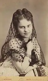 Photographie d'une jeune femme aux cheveux épinglés, portant une robe blanche et un foulard partiellement transparent.