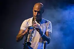 un Noir-Américain en tee shirt blanc, sur une scène baignée de fumée, jouant du saxophone soprano