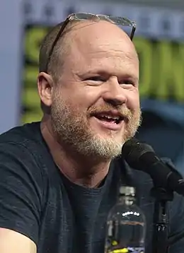 Visage d'un homme blanc, avec une légère barbe rousse, portant un T-shirt brun, avec un micro en premier-plan