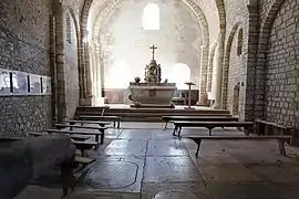 Intérieur de la chapelle éclairée uniquement par les ouvertures du fond. Le sol est couvert de pierres tombales.