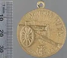 Photo d'une médaille dorée représentant un canon, le soleil se levant en arrière-plan.