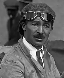 Photo en portrait américain de Jules Goux arborant sa casquette et ses lunettes de pilote, malgré sa tenue de ville.