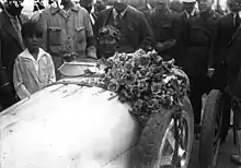 Photo d'une homme au visage noirci dans une voiture avec un bouquet de fleurs, entouré par la foule.