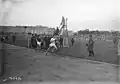 Photographie en noir et blanc d'une course à pied sur un stade en terre.