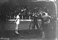 Photographie en noir et blanc d'un athlète se tenant debout devant des caméramans et photographes.