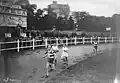 Photographie en noir et blanc d'une course à pied sur un stade en terre.