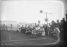 Photographie en noir et blanc d'un coureur à pied à l’arrivée d'une course, regardé par des spectateurs.