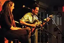 une femme assise sur un tabouret devant un guitariste sur scène