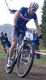  Homme à VTT portant une tenue bleu sombre avec une bande bleu-blanc-rouge sur la poitrine.