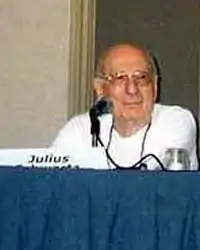 Photo d'un homme âgé assis à une tribune, avec devant lui un microphone