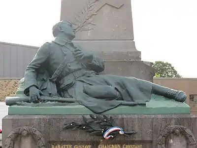 Monument aux morts de Juvigny-sous-Andaine (61140), Statue d'un poilu mourant couché (J. Dechin) se tient devant un obélisque surmonté d'une boule et d'un coq.