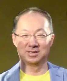 Portrait d'un homme brun d'origine asiatique protant des lunettes, habillé de bleu clair et de jaune.
