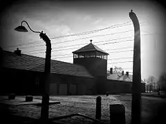 Photo en noir et blanc montrant derrière des barbelés un long bâtiment avec un mirador au milieu