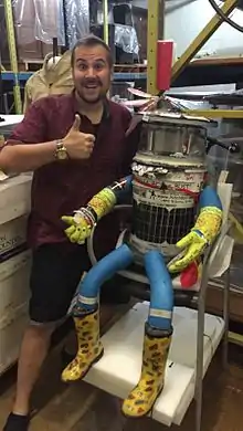 Un homme joyeux lève le pouce à gauche d'un robot humanoïde assis dans un fauteuil.