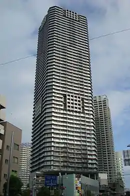 Ground-level view of a white, rectangular high-rise; the corners are cut and balconies form horizontal stripes up the height of the tower