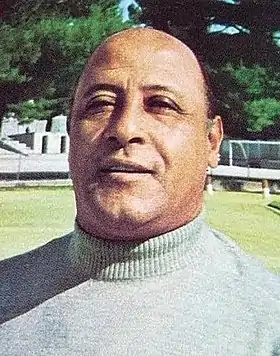 Photographie en couleur d'un homme vu de face en col roulé gris.
