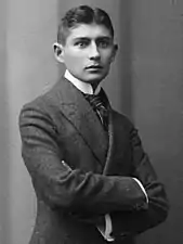 Portrait photographique noir et blanc d'un homme jeune prenant la pose, les bras croisés, et vêtu d'un costume gris.