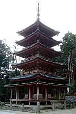 Une pagode à quatre étages avec poutres rouges vermillon et toit vert. Juste au-dessous du toit du premier étage il y a un toit supplémentaire ondulé.