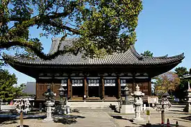 Wooden building with a hip-and-gable roof an a central staircase leading to the raised floor level.