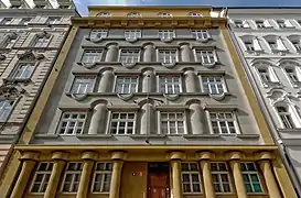 Façade sur rue bicolore, or au premier et dernier niveau, ainsi que sur le pourtour de la façade, gris en son centre (quatre étages), possédant des formes cylindriques (piliers décoratifs notamment).