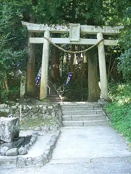 Photo couleur d'un portique de sanctuaire en pierre devant un escalier en pierre s'étendant dans une forêt.