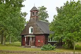Une chapelle en bois au milieu d'une prairie avec quelques arbres.