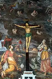Peinture murale montrant des personnages religieux. Un autel avec une crucifixion devant la fresque.