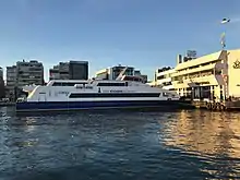 Photographie en couleurs, représentant un bateau et des bâtiments.