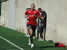 Photo de Karim Benzema effectuant un footing sur le bord de la pelouse avec le maillot de l'Olympique lyonnais.