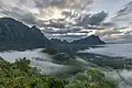 Montagnes karstiques, nuages colorés et brume au lever du jour, vue sud depuis le sommet du mont Nam Xay, durant la mousson, à Vang Vieng.