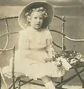 Photographie en noir et blanc d'une petite fille blonde assise et portant une robe blanche.