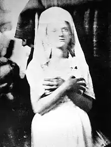 photographie noir et blanc d'une jeune femme très pâle, les bras croisés sur la poitrine