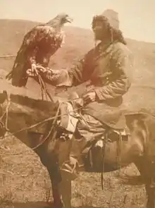 Photographie sépia d'un chasseur à cheval tenant un aigle.