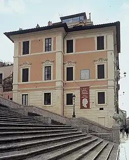 Deux grandes maisons côte à côte, mais légèrement décalées l'une de l'autre, peintes en ocre et rose, à droite des escaliers (en montant) ; trois étages, trois piliers de soutènement