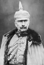 Photo en noir et blanc d'un homme en manteau militaire, moustache à l'impériale et casque à pointe très haute.