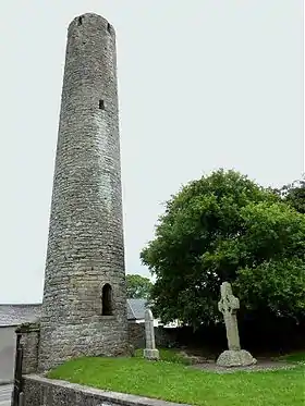 Les principaux vestiges restants du monastère médiéval de Kells : la haute tour monastique (aujourd'hui amputée de sa toiture conique), conforme à la typologie habituelle des round towers irlandaises, avec à son pied la croix sculptée dite « de St Patrick et St Colomba ».