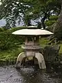 Yukimi-dōrō à trois pieds. Un pied repose à terre, les deux autres dans l'eau.