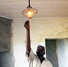 Eleveur laitier kényan allumant une lampe à biogaz en tendant une allumette vers celle-ci, au plafond.