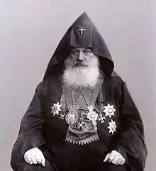 Photographie d'un homme à la barbe blanche, assis et portant une tenue cléricale arménienne.
