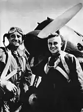 photo en noir et blanc de deux hommes souriants en tenue de pilote devant un avion