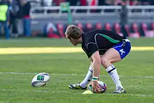 Kieran Marmion accroupi ramassant un ballon à l'échauffement