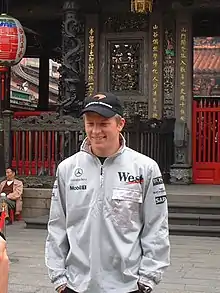 Photo d'un homme souriant, en survêtement, devant un bâtiment traditionnel taïwanais