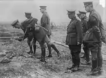 photographie du roi, portant un uniforme d'officier britannique, est entouré d'officiers dont l'un tient un obus à la main