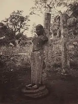 Photo monochrome d'une statue sans bras appuyée sur une colonne parmi des arbres.