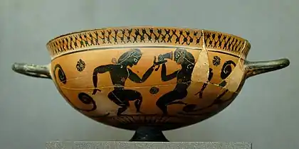 Scène de komos, procession rituelle festive. Danseurs nus, jeune homme et homme mûr. Coupe attique à figures noires v. 560. D. 16,2 cm. Louvre