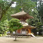 A two-storied pagoda shaped tower with a square base and a round upper story. The walls are faded white and the beams faded red.