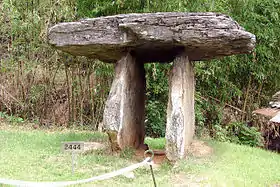 Photographie d'un dolmen prise en extérieur. Un pierre plate est posée sur deux autres pierres debout, elles aussi plates.